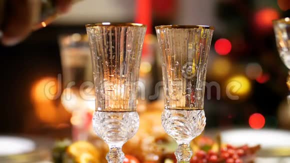 特写慢镜头视频在两个玻璃杯中倒入香槟以对抗发光的圣诞灯和燃烧的壁炉视频的预览图