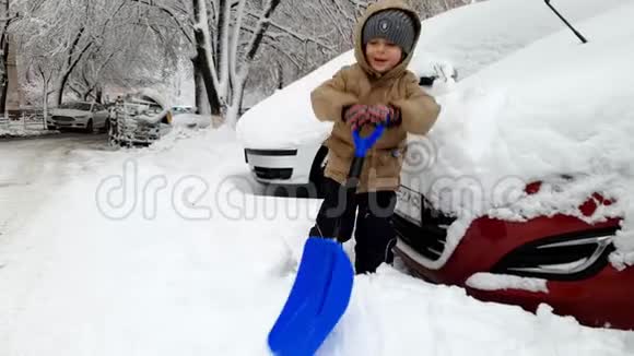4k镜头快乐微笑的幼儿男孩用大雪铲在停车场上挖雪堆视频的预览图
