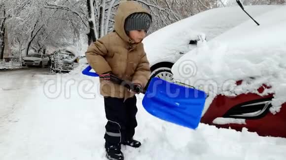 雪灾后小男孩在雪地里锯车的4K镜头孩子用铲子挖雪视频的预览图