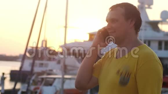 年轻微笑的胖子在夕阳下的海船上用手机说话镜头耀斑效果3840x2160视频的预览图