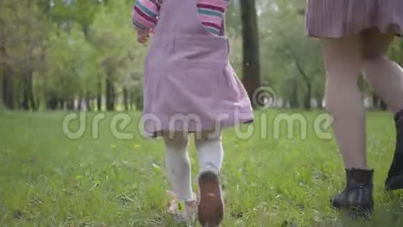 年轻的妈妈和小女孩的腿在公园里奔跑在绿草上紧紧地牵着手积极健康视频的预览图