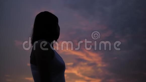 夕阳西下的天空中女性的剪影双手举起女性身体的黑色阴影少女在户外玩得开心视频的预览图
