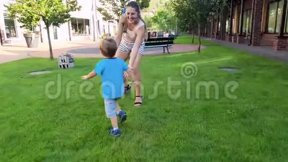 带着年轻母亲在公园里散步在玩具木屋里看着的快乐微笑的幼儿男孩的4k镜头视频的预览图