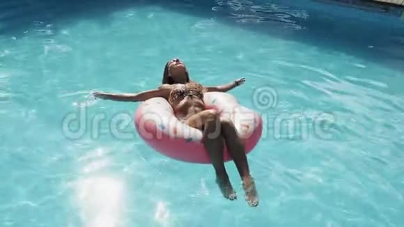 女人在泳池里尽情享受充气的粉色甜甜圈视频的预览图