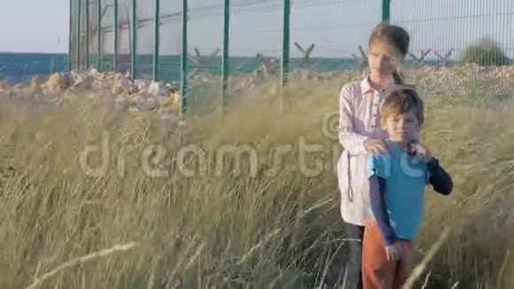 高围栏近海兄妹站在一起等待帮助大风吹过草地吹过哭泣的孩子们视频的预览图
