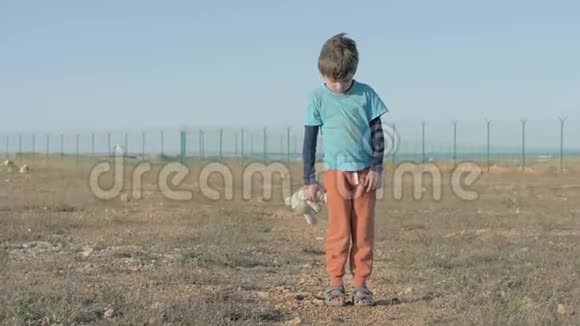 孤儿在难民营地区被遗弃的孤独儿童穿着脏衣服的男孩拿着玩具毛绒兔子无家可归的小东西视频的预览图