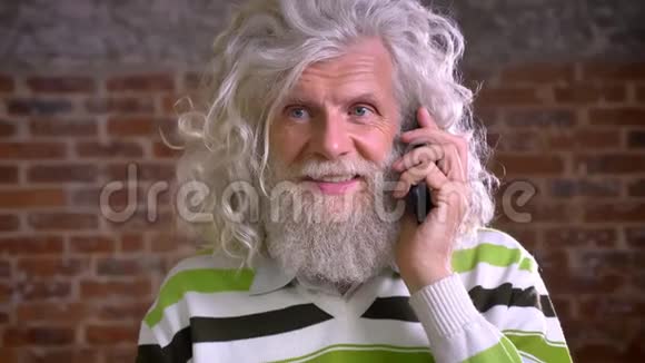 在电话中平静地交谈老白种人留着大白胡子和波浪发集中精力打电话站在那里视频的预览图