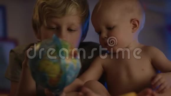 可爱的孩子只是坐在坏的地方玩地球仪他的兄弟用流动相机做伙伴视频的预览图