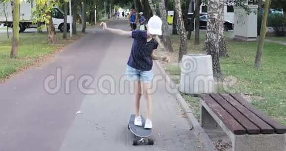一个戴着帽子的可爱女孩在公园的滑板上滑冰视频的预览图