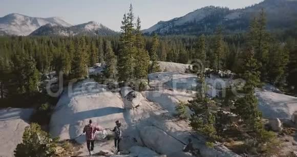 无人机镜头跟随年轻的快乐夫妇一起奔跑一起在令人惊叹的白色岩石上徒步走向史诗般的约塞米蒂公园天际线视频的预览图