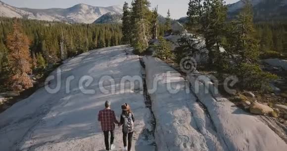 空中跟踪拍摄的年轻浪漫夫妇拥抱一起徒步旅行在惊人的白色岩石在约塞米蒂公园森林视频的预览图