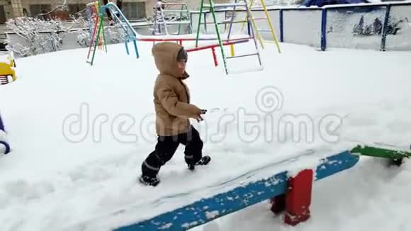 雪后在公园的操场上蹒跚学步的男孩在雪地上行走和攀爬的4k镜头视频的预览图