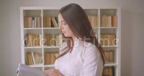 一位年轻漂亮的白种人女学生在图书馆里看书和看照相机的特写镜头视频的预览图