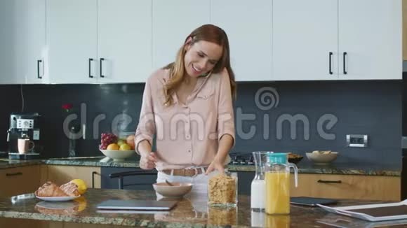 快乐的女人准备健康的早餐放松的人在手机上说话视频的预览图