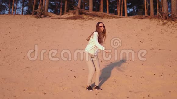 年轻女子在春日的河滩上穿着白色的沙丘慢悠悠地欣赏日落视频的预览图