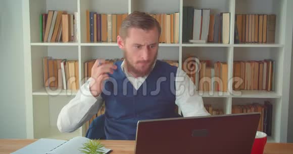 年轻的高加索商人用笔记本电脑在办公室里用书架做笔记的特写照片视频的预览图