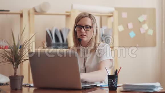 女孩白种人坐在笔记本电脑前引导头戴耳机上的对话并写下了视频的预览图
