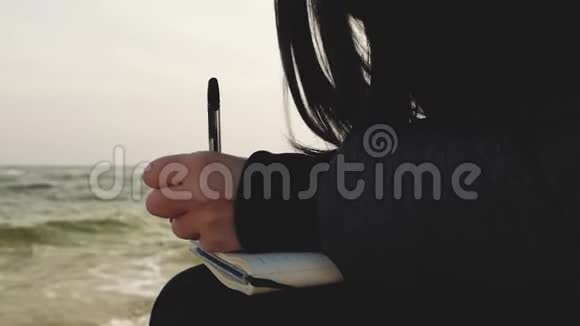 女孩在一本笔记本上写字笔在大海的背景上视频的预览图