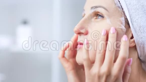 美丽的年轻女子将白色纺织面膜敷于面部肌肤清洁毛孔视频的预览图