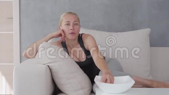 一个女人坐在柔软的沙发上吃着爆米花看着电视屏幕完全沉浸在情节和是什么视频的预览图
