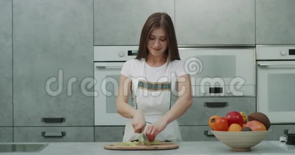 一个年轻的女人在镜头前切了一些蔬菜在一个令人惊叹的灰色厨房里有着现代的设计视频的预览图