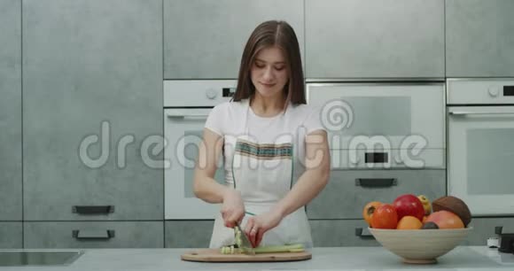 在一个现代化的厨房里微笑着美丽的女性非常快地在镜头前切了一些蔬菜微笑着可爱地看着视频的预览图