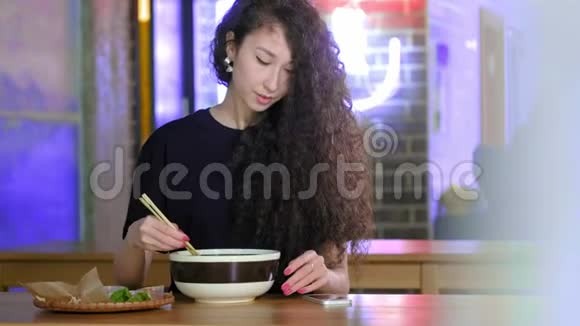 一个可爱的年轻亚洲女孩在亚洲咖啡馆的智能手机pho汤上拍照中文越南文或日文视频的预览图