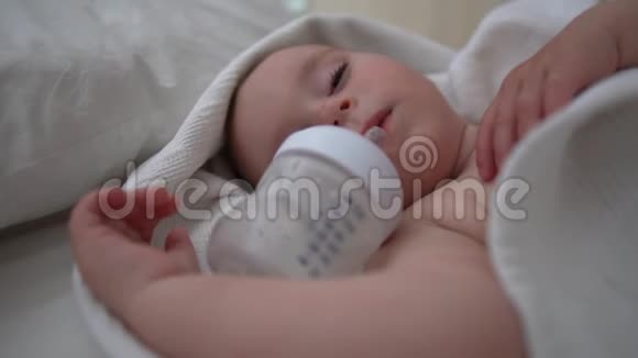 一个睡着的带空瓶子的可爱宝宝躺在床上床上铺着白色的床上用品视频的预览图
