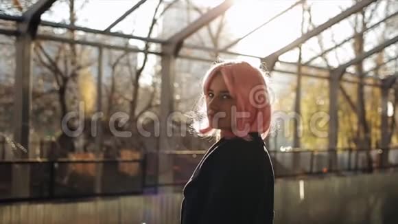 美丽的白种人年轻女孩粉红色的头发和黑色的外套站在火车站站着的漂亮女人视频的预览图