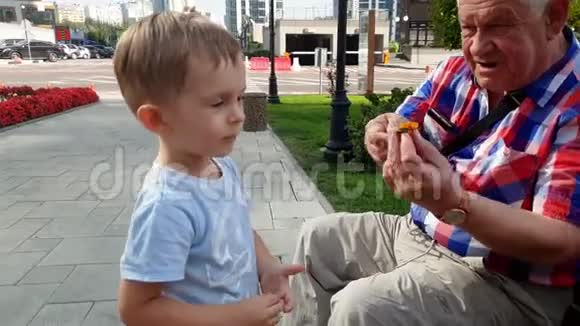 4k视频老爷爷在公园的长椅上玩玩具和他蹒跚学步的孙子视频的预览图