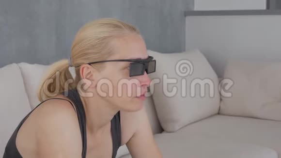一个女人在柔软的沙发上吃爆米花看着3D眼镜里的电视屏幕视频的预览图
