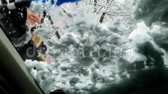 来自汽车司机座位的4k视频年轻微笑的女人在暴风雪后清理汽车挡风玻璃视频的预览图