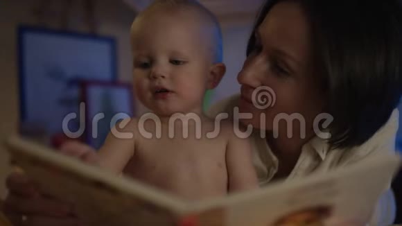 妈妈给躺在床上的漂亮宝宝看书给他看不同的照片视频的预览图