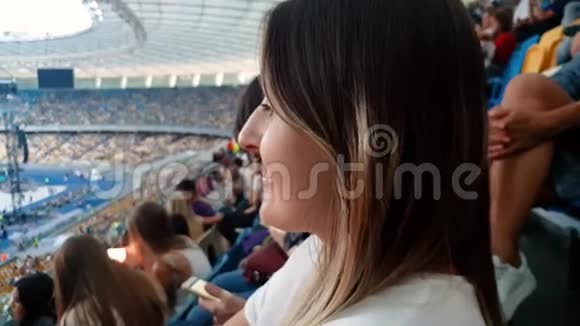4K特写视频美丽的微笑年轻女子长发坐在大体育场的法庭上观看视频的预览图
