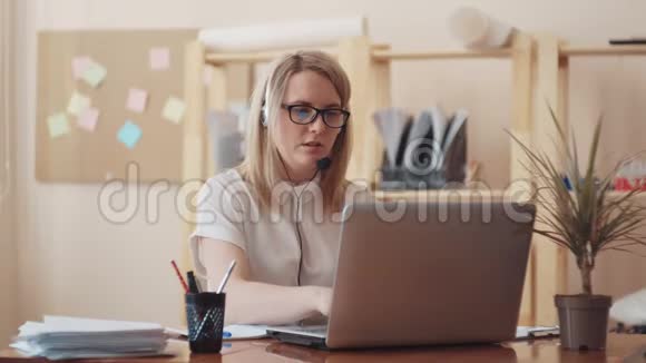 高加索女孩戴着眼镜坐在办公室里拿着笔记本电脑在麦克风上进行对话视频的预览图