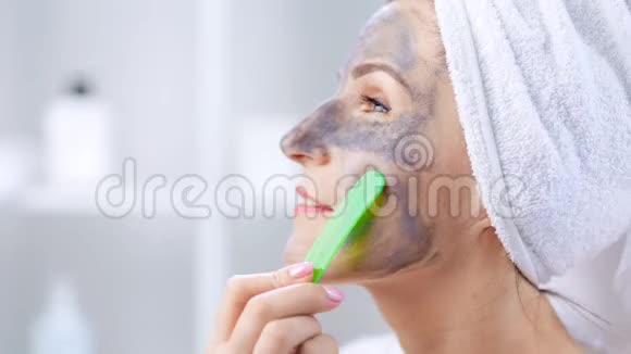 年轻女子用铲子把灰色的粘土面具戴在脸上视频的预览图