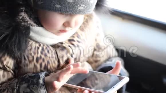 小女孩在路上在车里玩智能手机视频的预览图