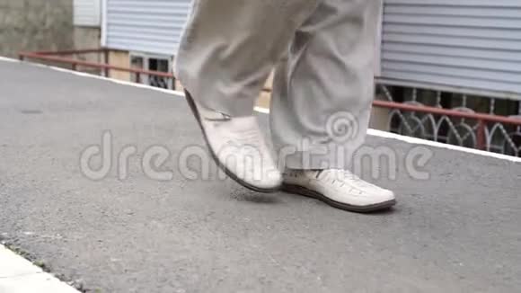 男人慢慢地自信地穿着白色的鞋子走在小镇的小径上视频的预览图