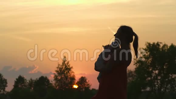 日落剪影年轻的母亲抱着她的孩子在城市公园站在夕阳面前生动视频的预览图