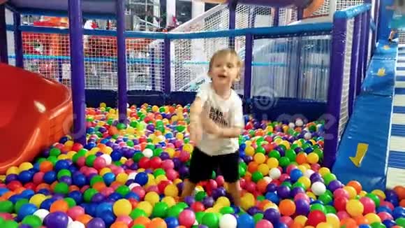 4k视频快乐微笑幼儿男孩在游乐场投掷彩色塑料球视频的预览图