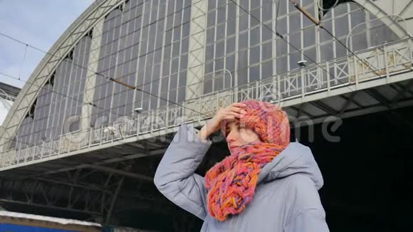 一位身穿蓝色外套头戴彩色帽子的年轻女子在晴朗寒冷的天气里在火车站的户外冬日画像视频的预览图