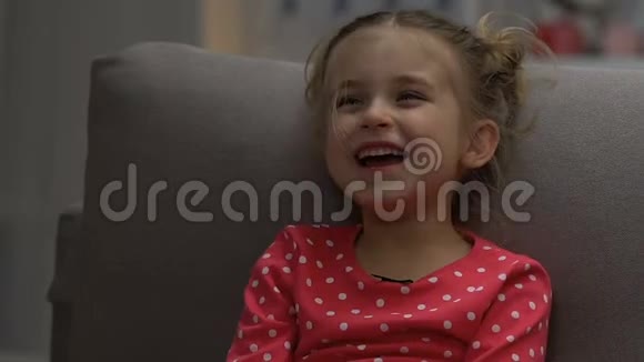 可爱的小女孩在晚上独自看喜剧节目笑着闭上眼睛视频的预览图