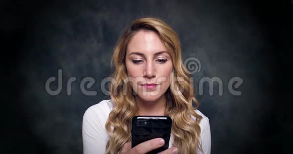 迷人的金发美女在黑暗的背景下通过手机说话视频的预览图