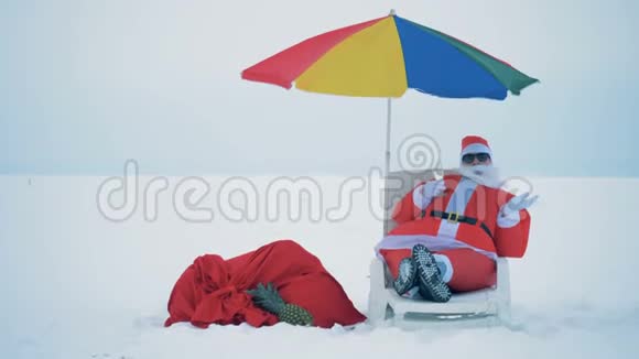 穿着圣诞老人服装的人坐在一张带着一杯香槟的躺椅上靠近视频的预览图