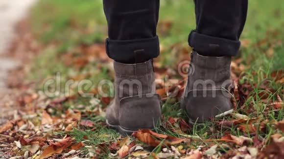 穿皮鞋的年轻人走在一条落叶的小路上秋天室外城市步行概念慢视频的预览图