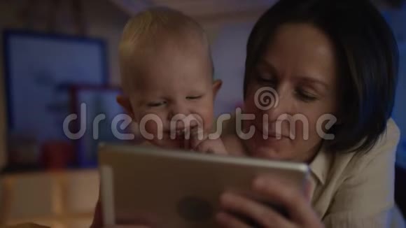 母亲在她的设备上看书给她的婴儿躺在床上上面有不同的照片并给他糖果视频的预览图