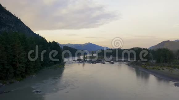 空中无人机在日落时看到树林之间的河流背景中的山脉视频的预览图