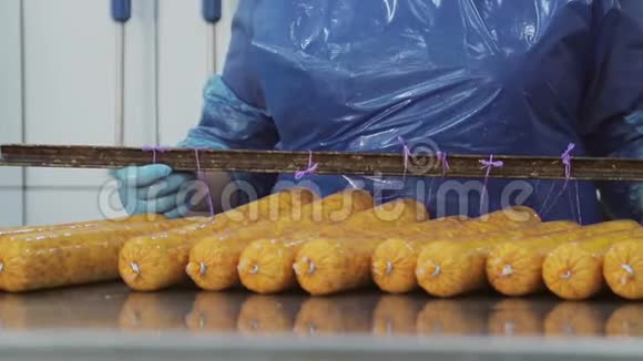 一个员工一个屠夫把新鲜的新鲜香肠挂在架子上以便在烤箱里进一步燃烧视频的预览图