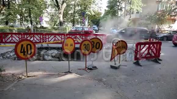 道路交通警告标志和一个塑料栅栏围绕着沥青的一个大洞蒸汽从那里出来视频的预览图