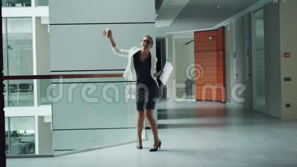 可爱的年轻女经理正在商务中心的大厅里跳舞拿着文件拿走咖啡享受自由视频的预览图